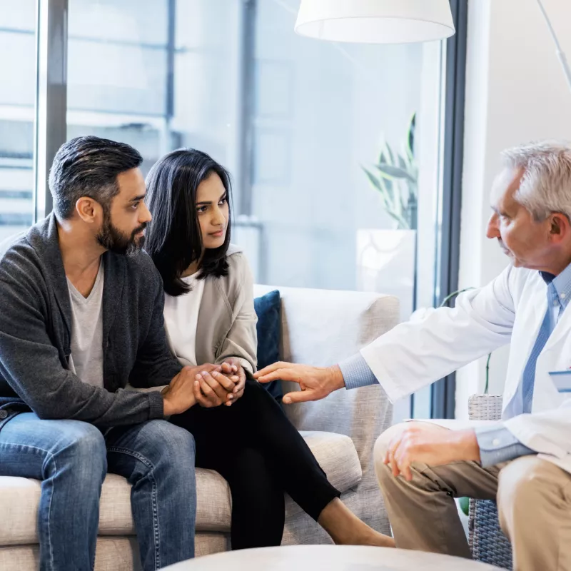 A couple, sitting with a doctor who is comforting them.