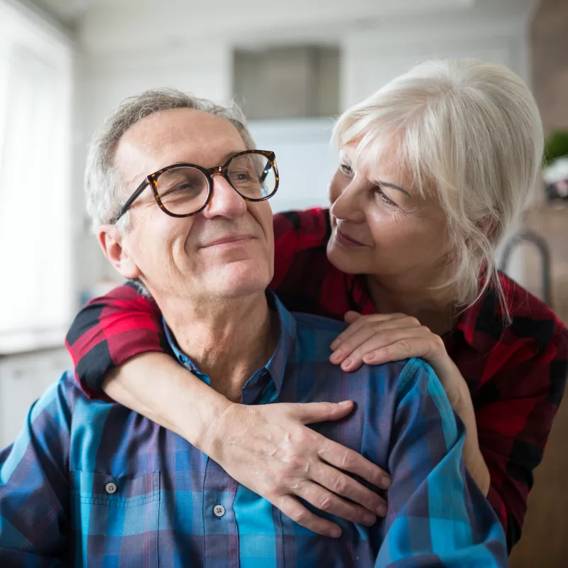 A senior man smiles at his wife as they embrace