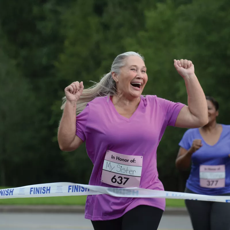 An older woman is ecstatic as she crosses the finish line of a charity foot race